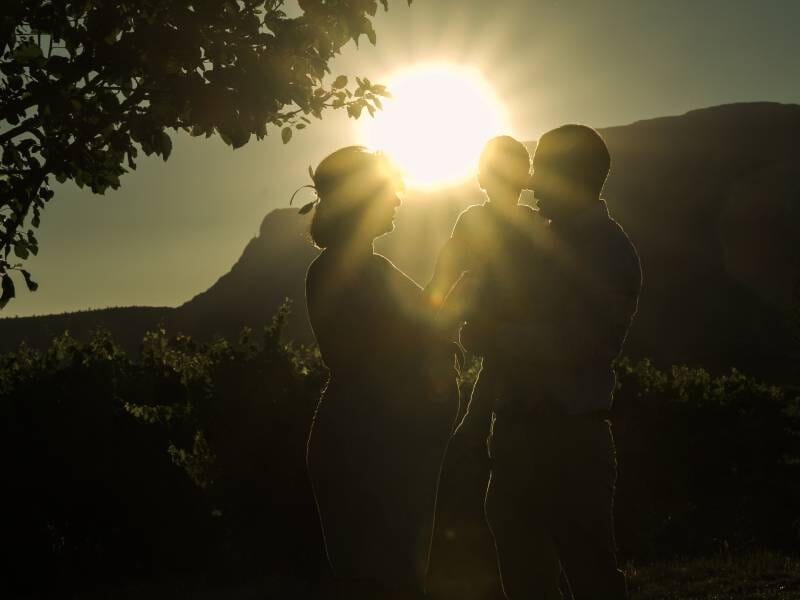 Silhouettes d'une famille avec un enfant, éclairées par un soleil couchant derrière des montagnes et des arbres.