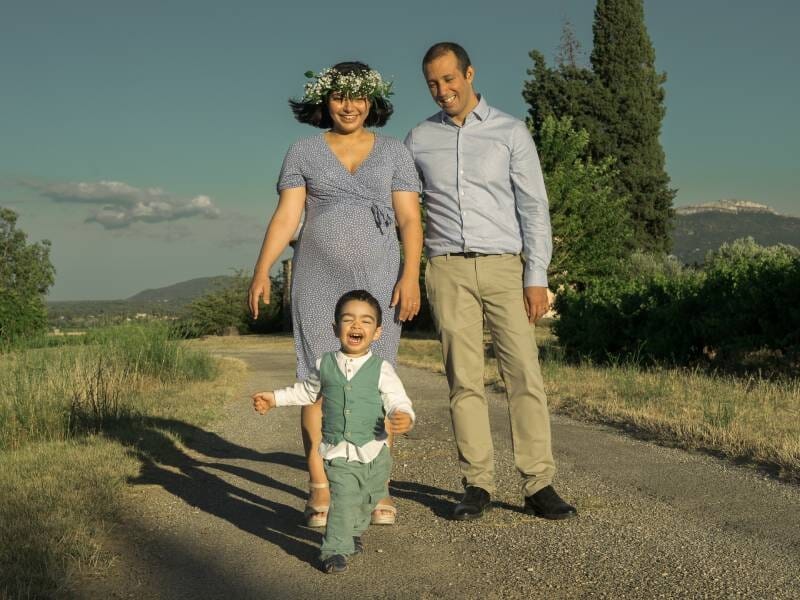Famille marchant sur un chemin en campagne, l'enfant souriant devant ses parents sous un ciel bleu clair, lors d'un shooting photo à Aix-en-Provence.