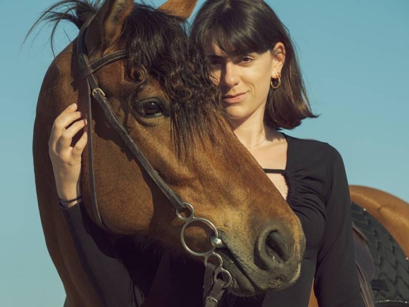 Jeune femme aux cheveux courts posant avec un cheval marron sous un ciel bleu clair, ambiance lumineuse, lors d'un shooting photo à Aix-en-Provence.