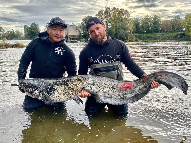 Deux pêcheurs debout dans l'eau tiennent un énorme poisson lors d'un stage de pêche près d'Agen.
