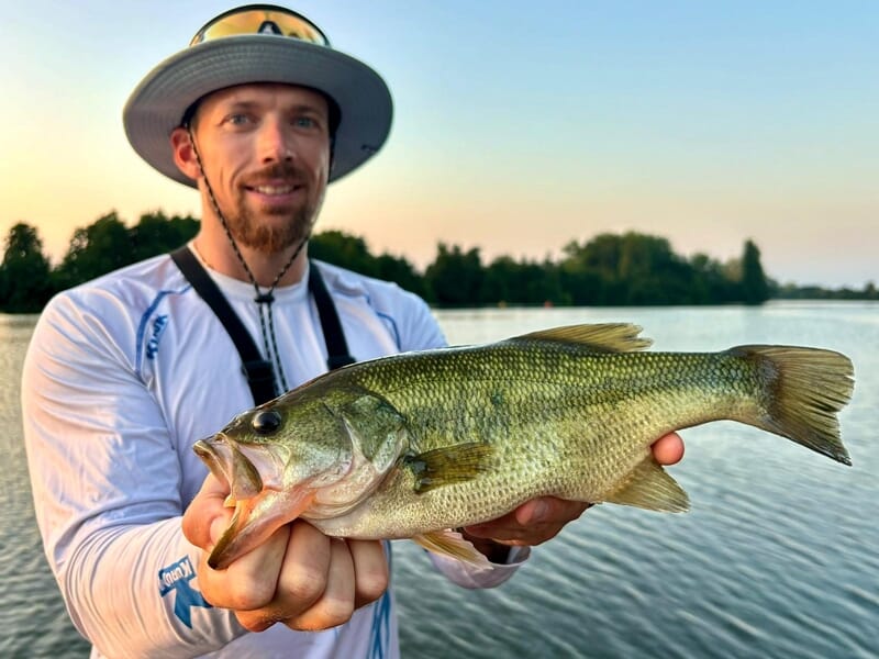 Un pêcheur avec un chapeau large tient un poisson vert lors d'un stage de pêche près d'Agen.