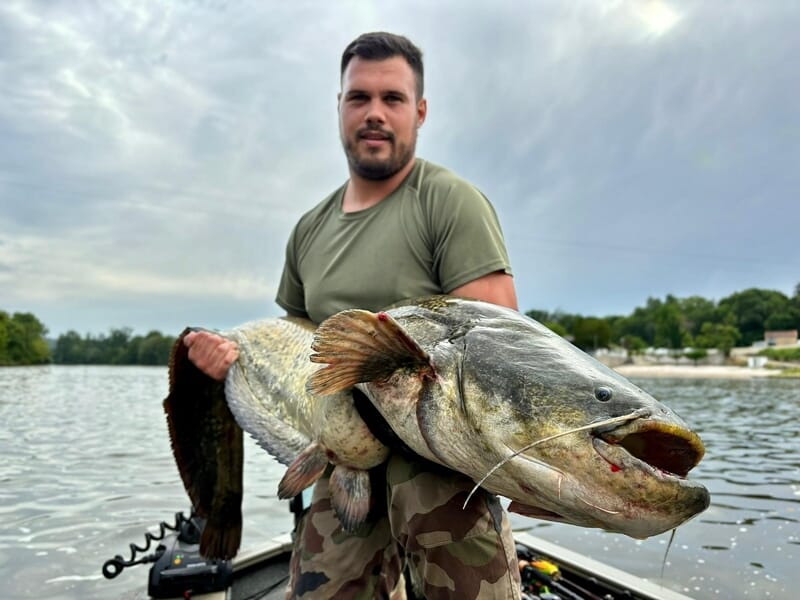Un homme en t-shirt vert tient un très gros poisson lors d'un stage de pêche près d'Agen.