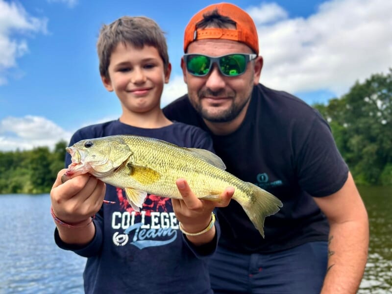Un enfant et un homme souriant montrent un poisson lors d'un stage de pêche près d'Agen.