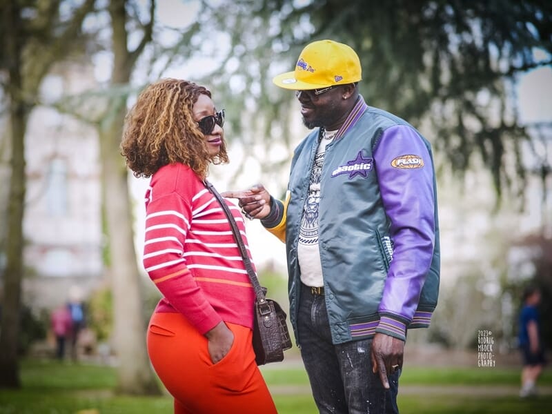 Deux personnes discutant dans un parc, l'homme en veste et casquette jaune lors d'un shooting photo grossesse au Mans.