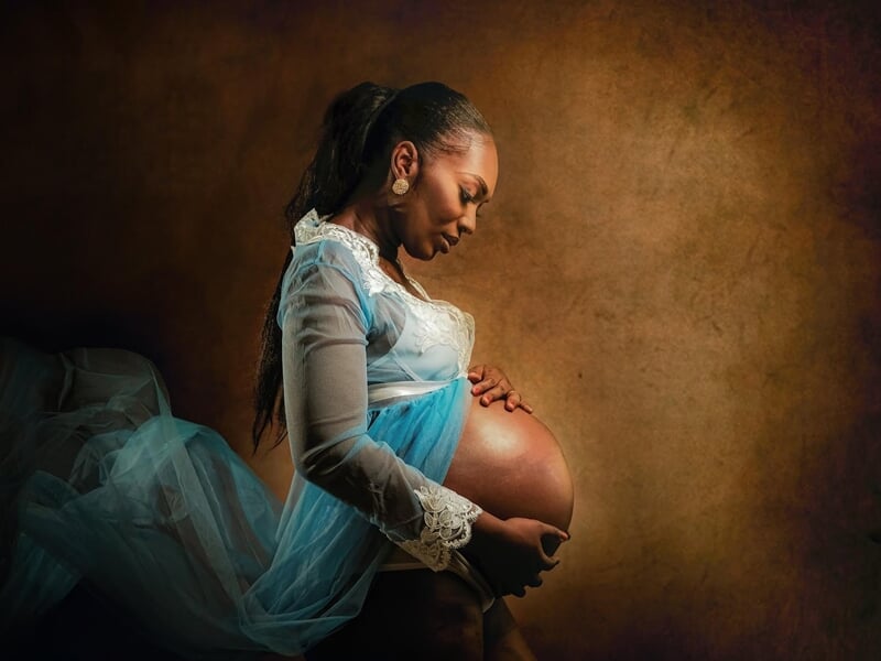 Femme enceinte en robe bleue et blanche, posant de profil avec les mains sur son ventre lors d'un shooting photo grossesse au Mans.
