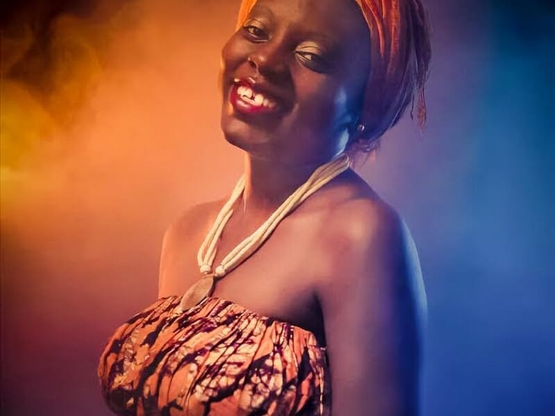 Femme souriante portant un bandeau orange et une robe colorée lors d'un shooting photo grossesse au Mans.