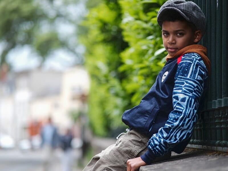 Jeune garçon appuyé contre un mur vert, portant une casquette grise et un blouson bleu lors d'un shooting photo portrait au Mans.