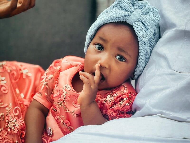 Un bébé en robe rose avec un turban bleu, regardant la caméra lors d'un shooting photo bébé au Mans.