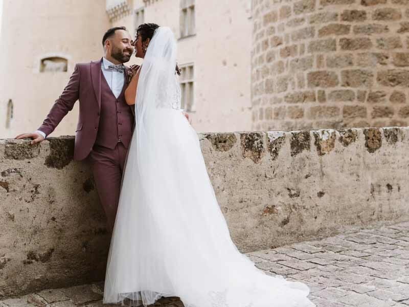 Jeune couple de mariés s'embrassant près d'un mur en pierre dans une ambiance romantique extérieure.