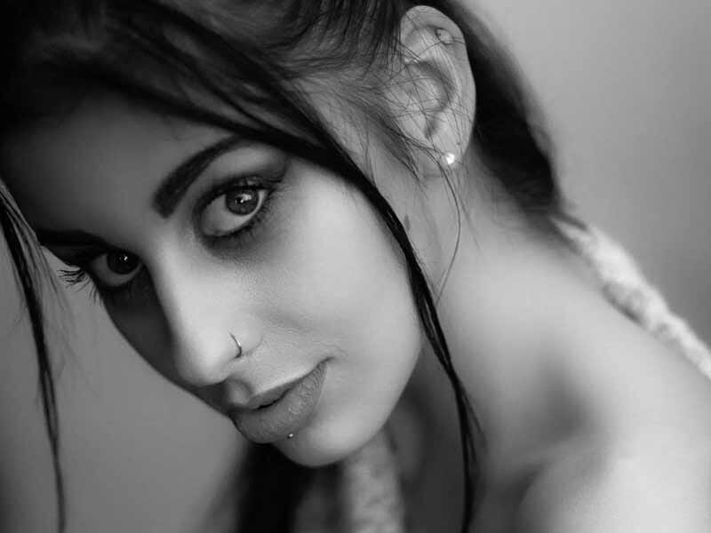 Portrait en noir et blanc d'une femme avec piercing au nez et lèvres, regardant l'objectif de près.