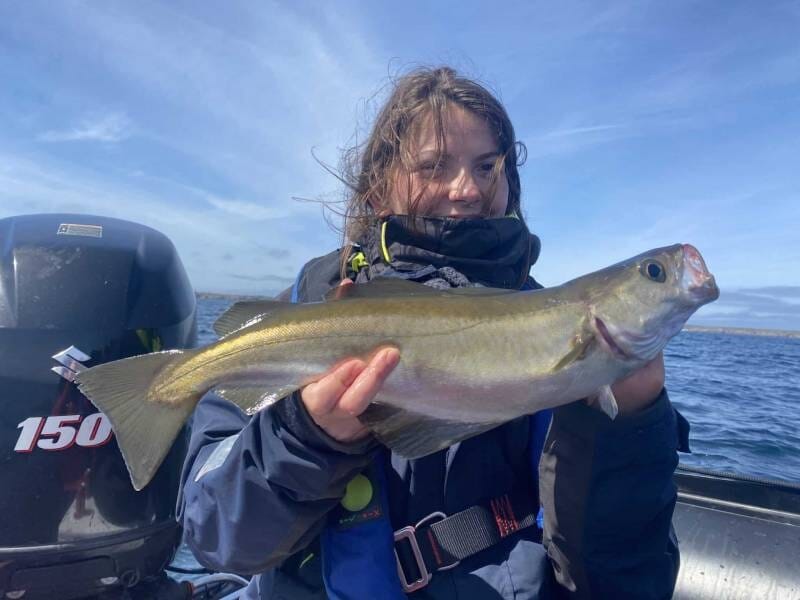 Femme souriante tenant un gros poisson fraîchement pêché sur un bateau en mer par temps clair et calme.