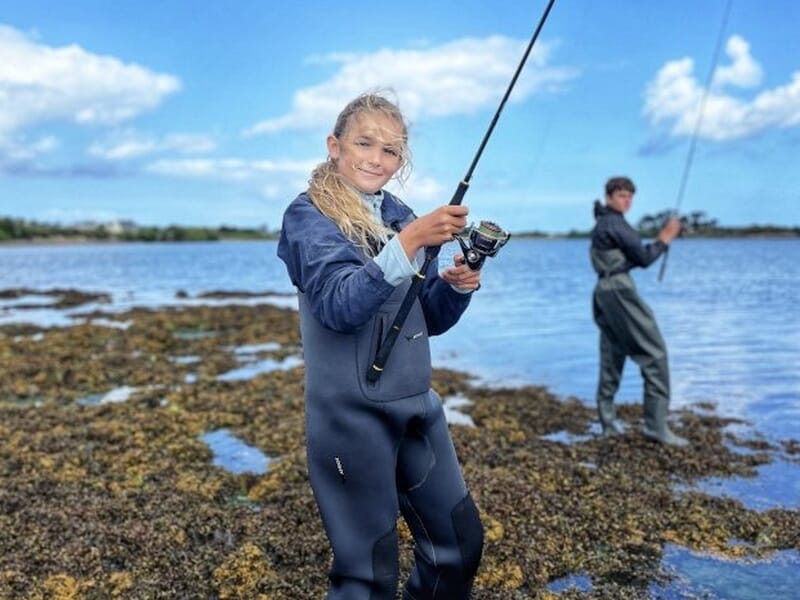 Jeune femme en combinaison de pêche tenant une canne à pêche lors d'un stage de pêche à Saint-Pol-de-Léon.