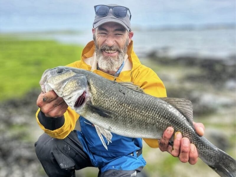 Homme barbu en veste jaune et bleue montrant un gros poisson lors d'un stage de pêche à Saint-Pol-de-Léon.