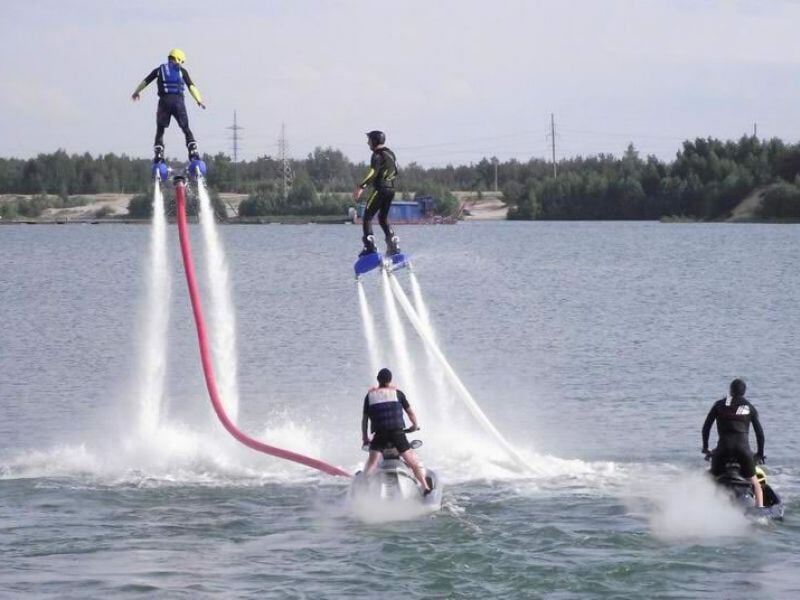 Deux personnes en flyboard sur un plan d'eau avec un ciel bleu et des arbres en arrière-plan