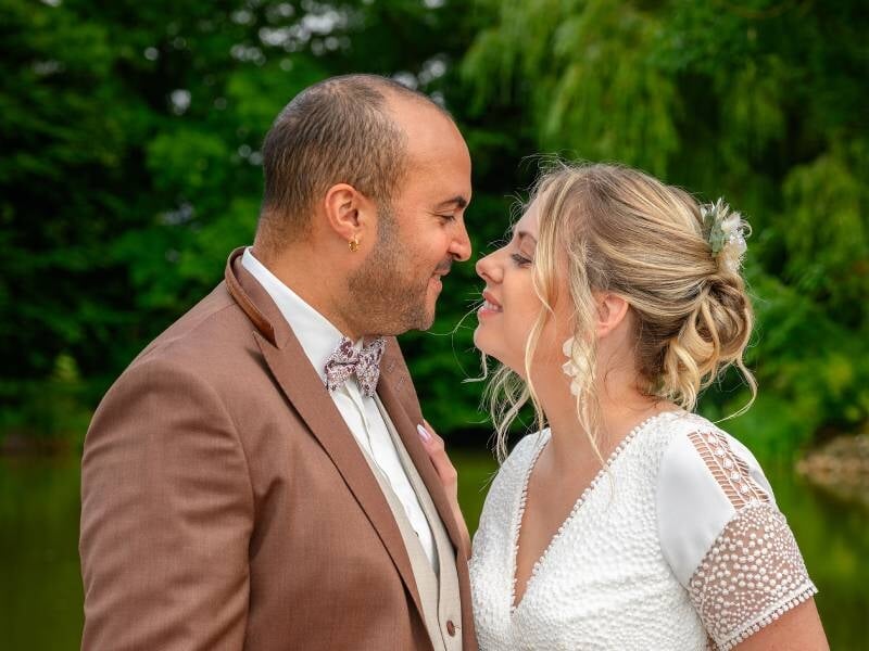 Un couple souriant se regarde tendrement lors d'une séance photo en extérieur dans un jardin verdoyant.