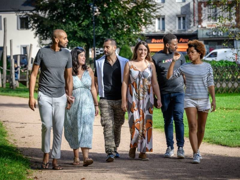 Groupe de six amis marchant ensemble dans un parc urbain par une journée ensoleillée, souriants et détendus.