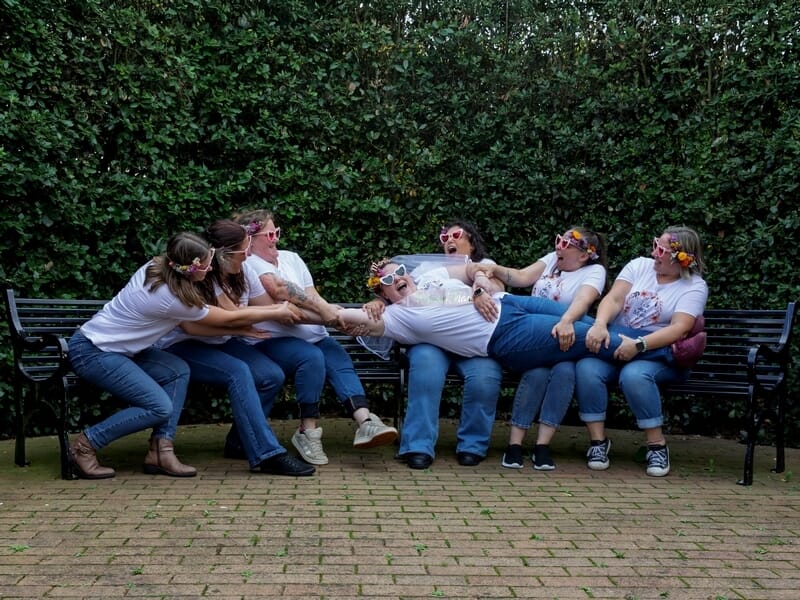 Amies en t-shirts blancs tirant une femme allongée sur un banc lors d'un shooting photo lifestyle à Caen.