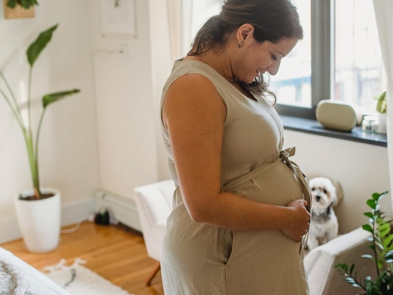 Femme enceinte souriante tenant son ventre dans un salon lumineux lors d'un shooting photo grossesse à Caen