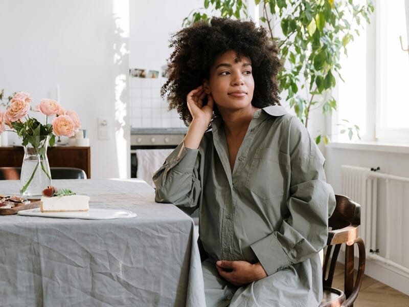 Jeune femme enceinte assise à une table près d'une fenêtre lors d'un shooting photo grossesse à Caen