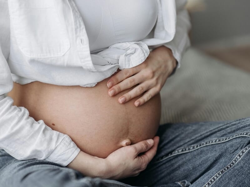 Gros plan sur un ventre de femme enceinte avec les mains posées dessus lors d'un shooting photo grossesse à Caen