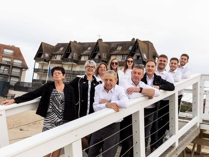 Groupe de dix personnes posant sur une passerelle en bois avec des maisons en arrière-plan lors d'un shooting photo de famille à Caen.