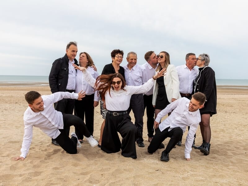Dix personnes s'amusant sur une plage, certains dansent et d'autres s'embrassent lors d'un shooting photo de famille à Caen.