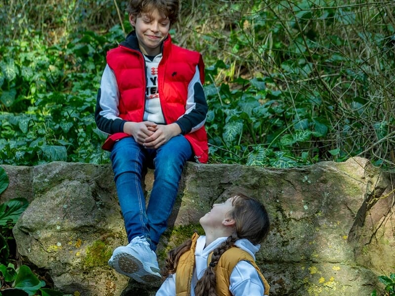 Deux enfants discutent assis sur un rocher dans un cadre naturel verdoyant lors d'un shooting photo de famille à Caen.