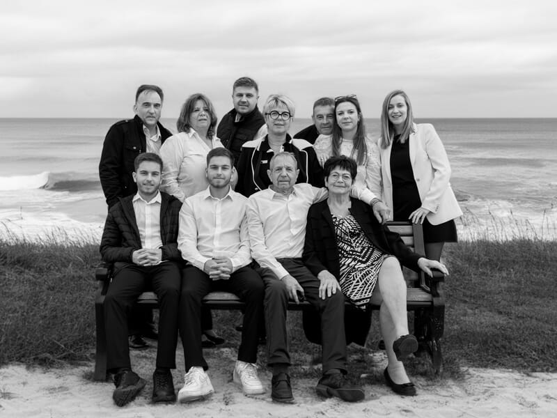 Groupe de dix personnes posant sur un banc face à la mer lors d'un shooting photo de famille à Caen.