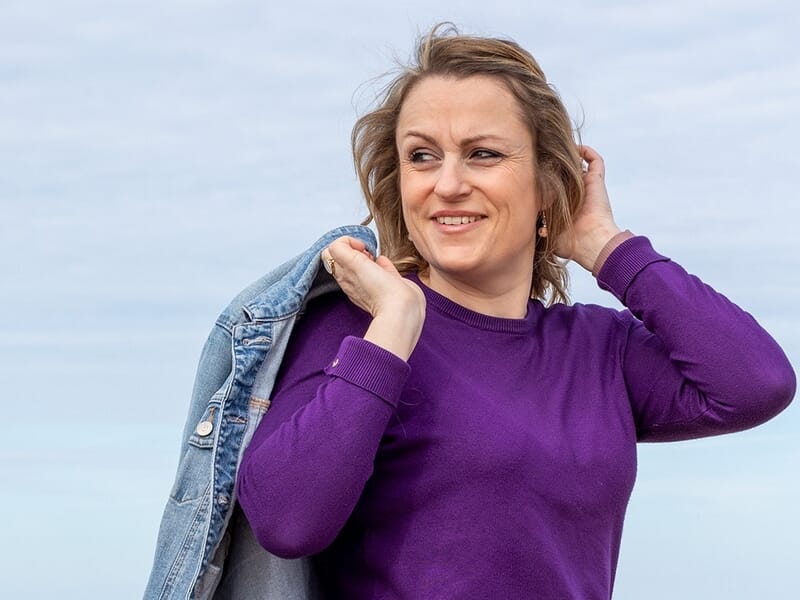 Femme souriante en pull violet tenant une veste en jean sur l'épaule, lors d'un shooting photo portrait à Caen.