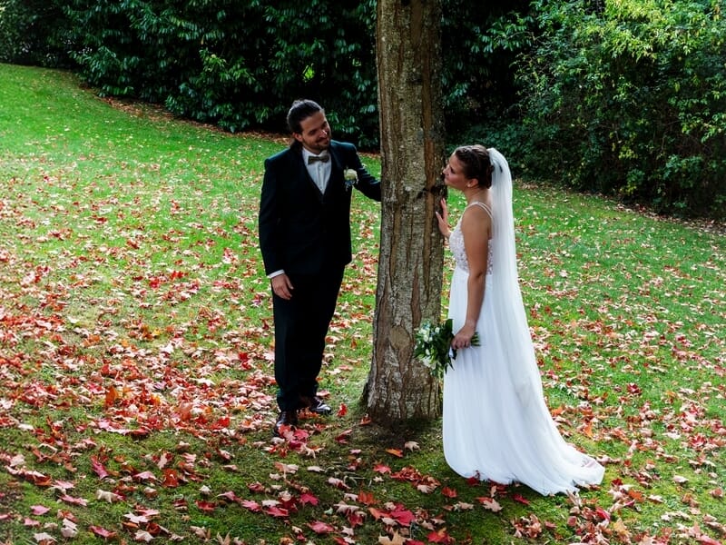 Un couple de mariés pose joyeusement près d'un arbre lors d'un shooting photo à Caen.