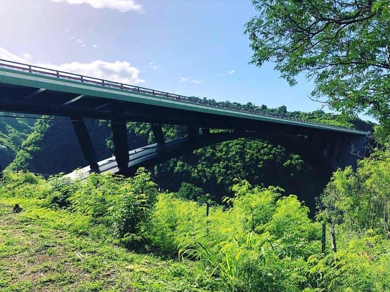 Un pont suspendu au-dessus d'une vallée verdoyante sous un ciel bleu avec quelques nuages blancs.