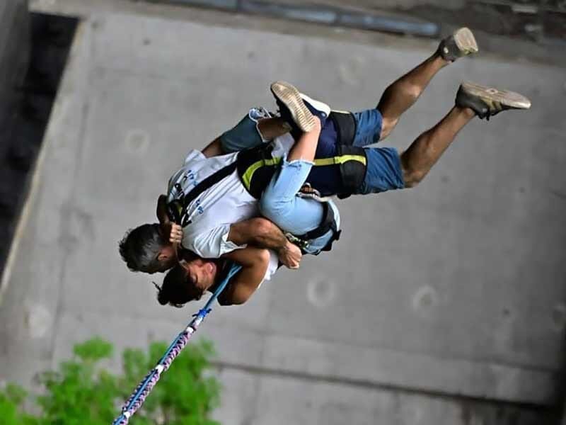 Deux personnes attachées ensemble en plein saut à l'élastique, suspendues la tête en bas.