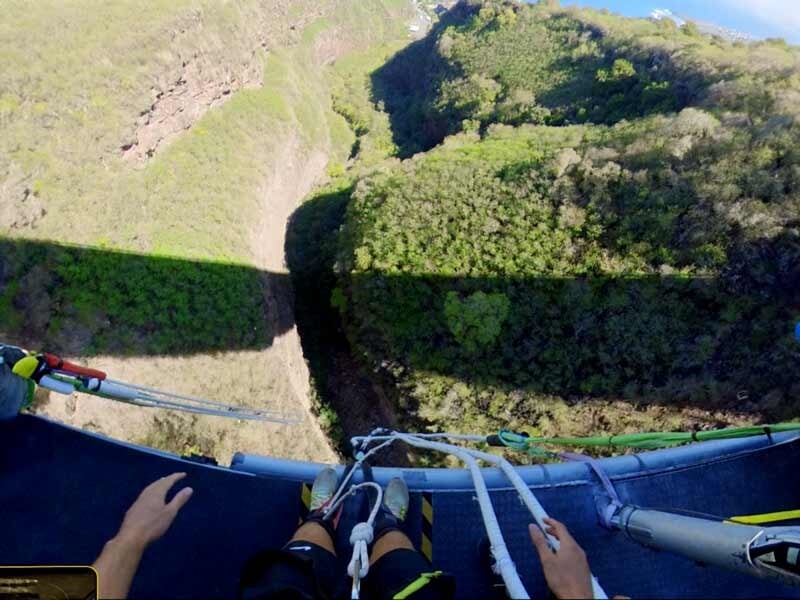 Vue plongeante depuis un pont sur des mains et des pieds prêts à sauter à l'élastique au-dessus d'une gorge boisée.