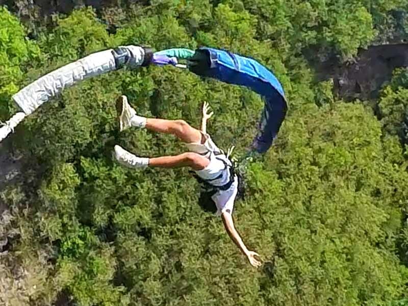 Saut à l'élastique en plein mouvement avec une personne en short blanc et tee-shirt, paysage vert en arrière-plan.