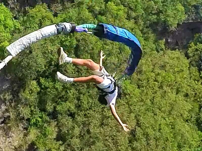 Saut à l'élastique en plein mouvement avec une personne en short blanc et tee-shirt, paysage vert en arrière-plan.
