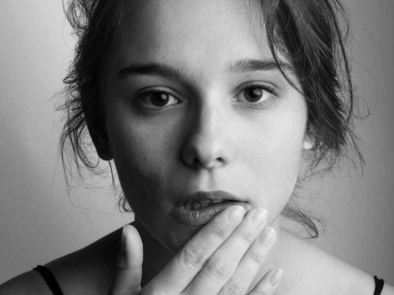 Portrait en noir et blanc d'une femme avec la main sur la bouche, regardant l'appareil avec une expression sérieuse.