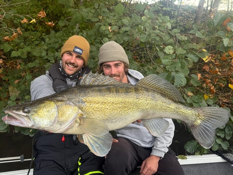 Deux hommes souriants tenant ensemble un grand poisson doré lors d'un stage de pêche en bateau sur la Seine à Poissy.