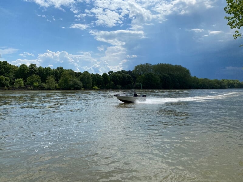 Bateau rapide sur une rivière large avec des arbres verts et un ciel partiellement nuageux lors d'un stage de pêche en bateau sur la Seine à Poissy.