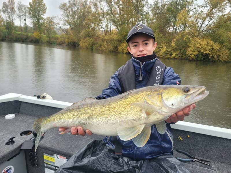 Jeune garçon en veste bleue tenant un poisson doré lors d'un stage de pêche en bateau sur la Seine à Poissy.