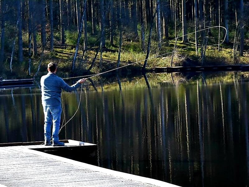 Un homme en jean pêche au lancer sur un ponton en boislors d'un stage de pêche à Autun.