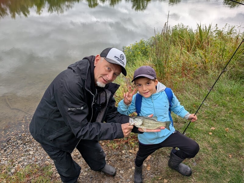 Un moniteur de pêche et un enfant souriant montrent un poisson fraîchement pêché lors d'un stage de pêche.