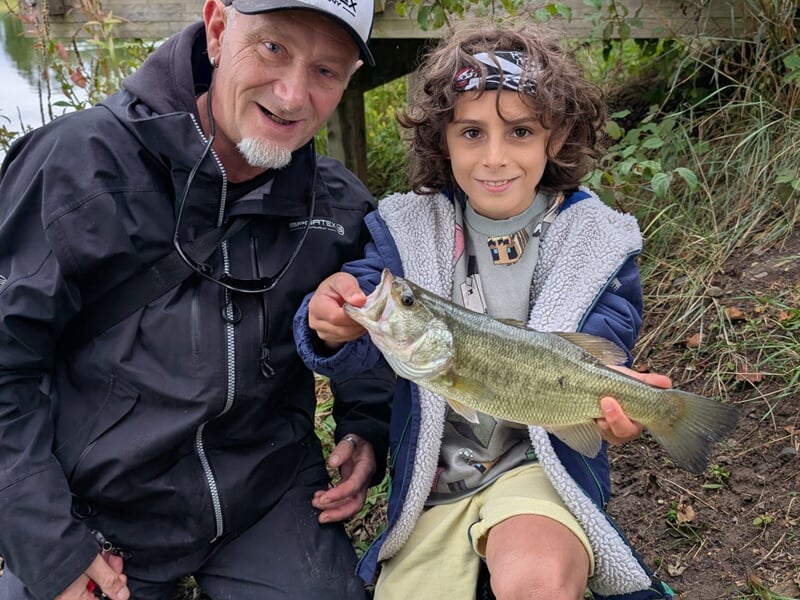 Un garçon heureux tient un poisson avec l'aide d'un moniteur de pêche lors d'un stage de pêche.