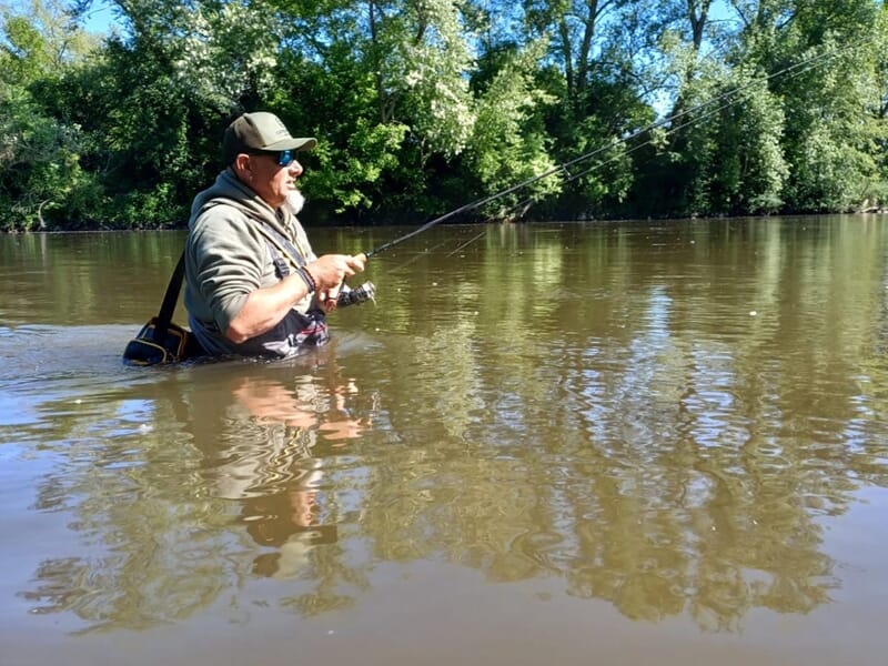 Un homme pêche dans une rivière, debout dans l'eau jusqu'aux cuisses, lors d'un stage de pêche à Vichy.