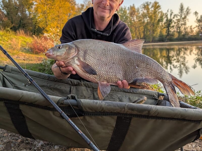 Un pêcheur montre fièrement un gros poisson tenu à deux mains.