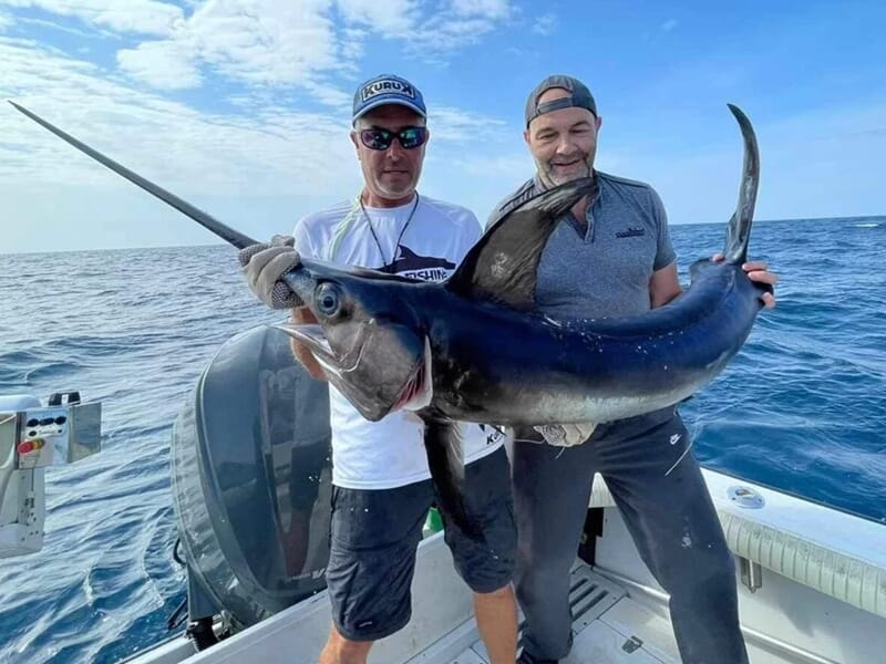 Deux hommes sur un bateau tenant un grand poisson pêché en mer lors d'une sortie pêche à Saintes-Maries-de-la-Mer.