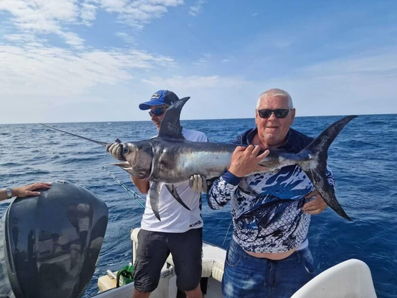 Deux hommes sur un bateau tenant un poisson de grande taille lors d'une sortie pêche à Saintes-Maries-de-la-Mer.
