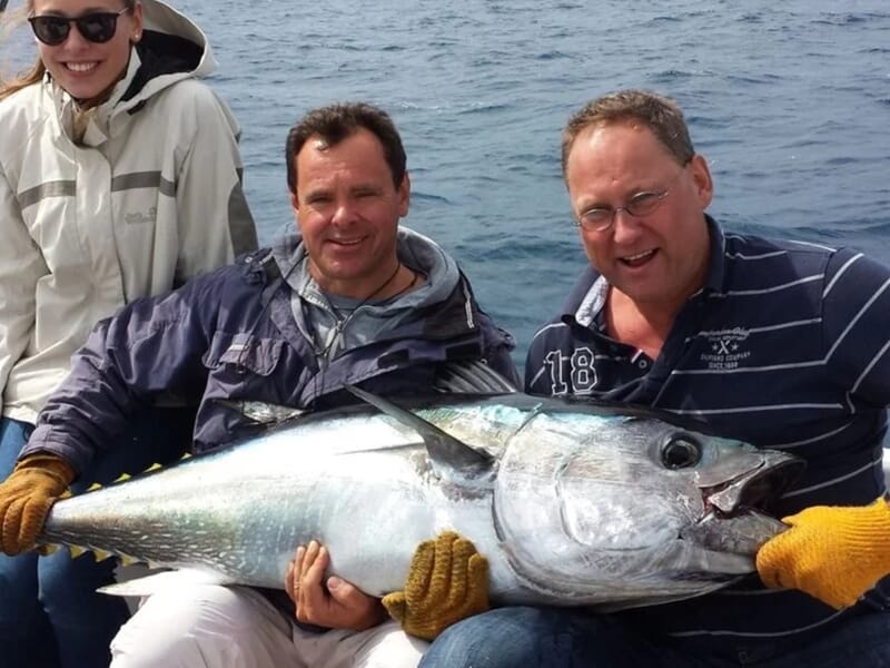 Trois personnes sur un bateau tenant un gros poisson argenté, tous souriants lors d'une sortie pêche à Saintes-Maries-de-la-Mer.