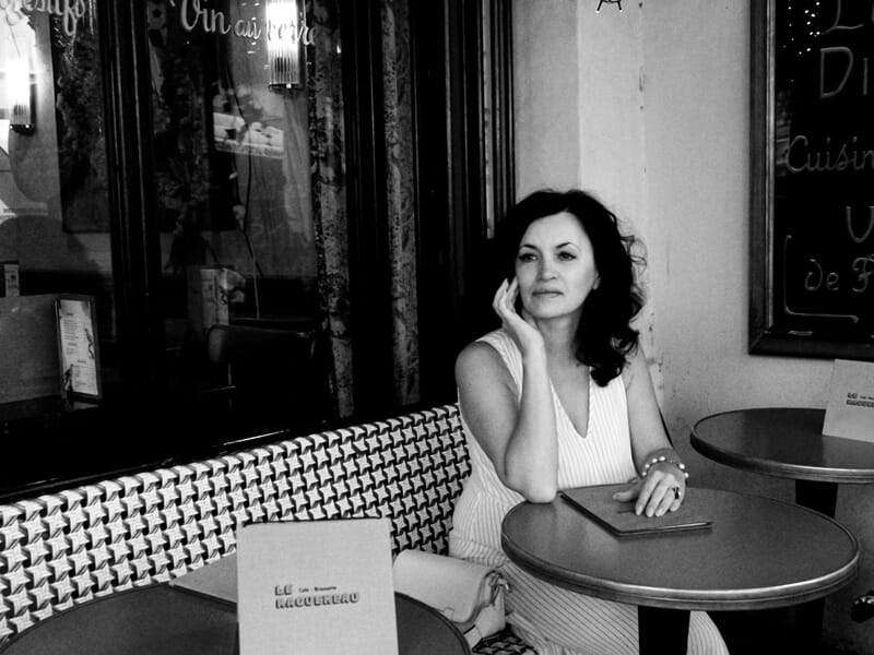 Femme assise seule à une table de café, regard pensif, ambiance en noir et blanc lors d'un shooting photo portrait à Maisons Laffitte.