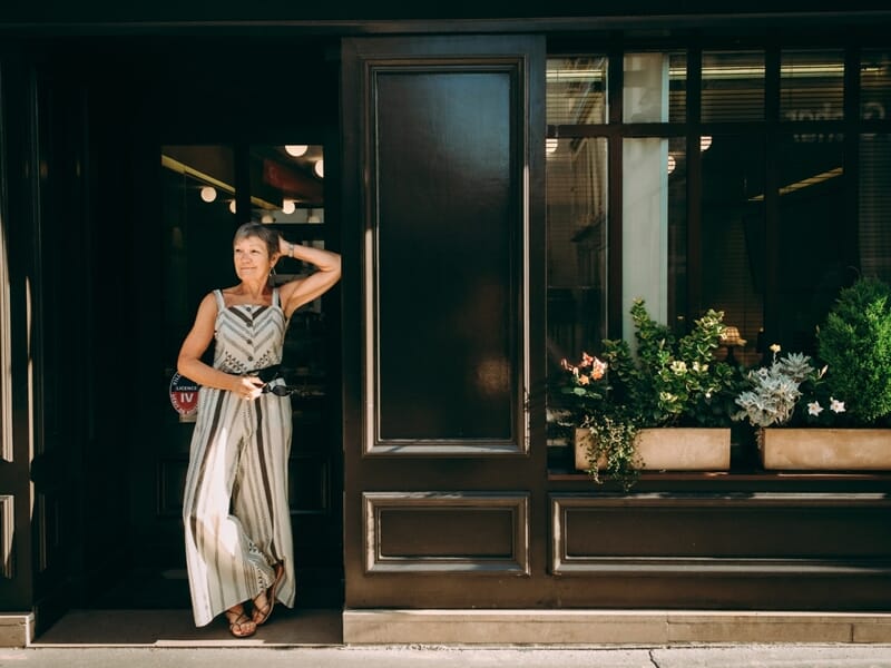 Femme debout devant une porte en bois sombre, vêtue d'une robe rayée lors d'un shooting photo portrait à Maisons Laffitte.