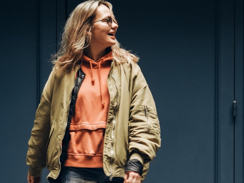 Jeune femme souriante en veste kaki et sweat à capuche orange lors d'un shooting photo portrait à Maisons Laffitte.